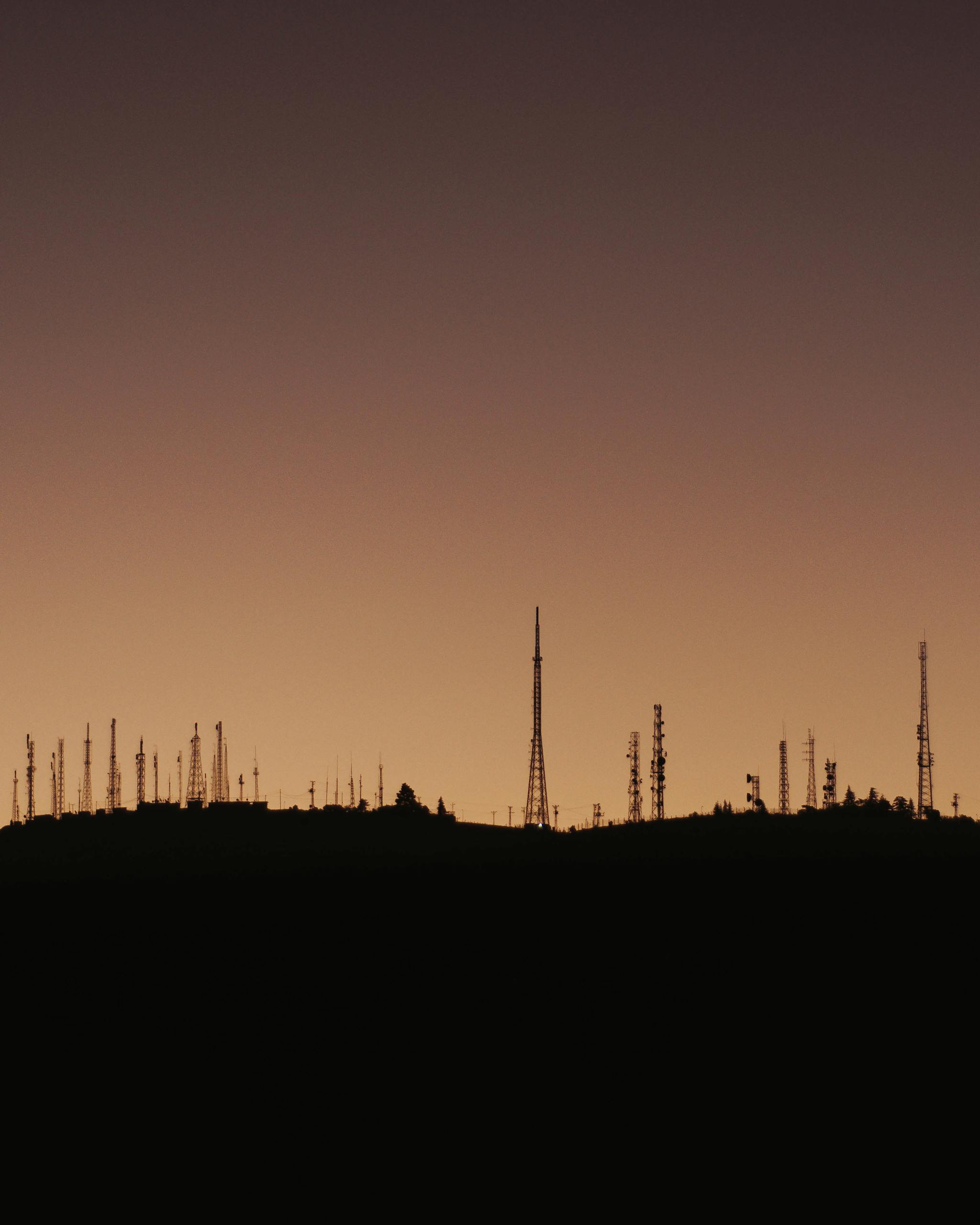 A serene silhouette of communication towers against a vibrant sunset sky, capturing the essence of twilight.